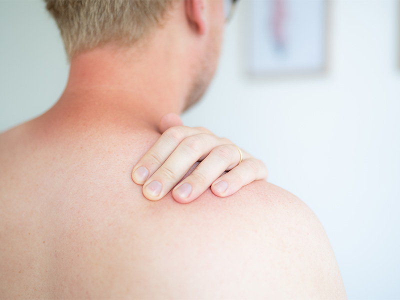 Patient hält seine Hand im Rücken am hernierten Triggerpunkt